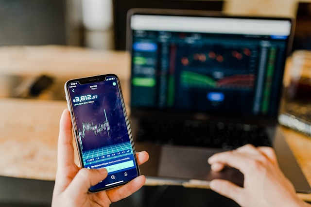 Pessoa analisando um celular e um laptop em tela de investimentos